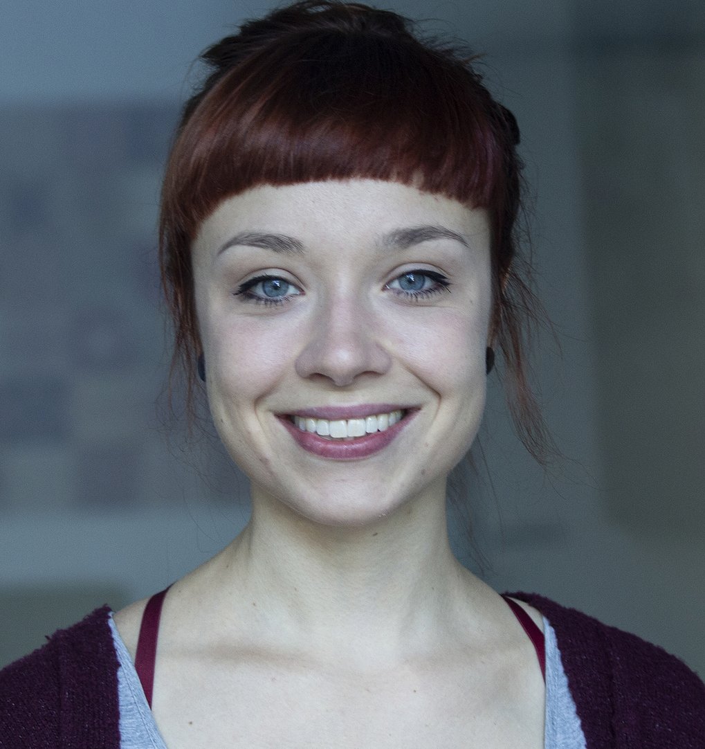 A smiling woman with red hair and blue eyes, wearing a gray top and a burgundy cardigan.