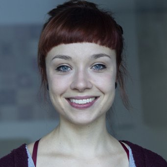 A smiling woman with red hair and blue eyes, wearing a gray top and a burgundy cardigan.