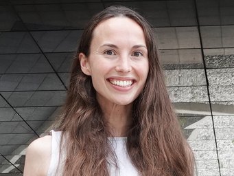 A smiling woman with long hair stands in front of a reflective surface.