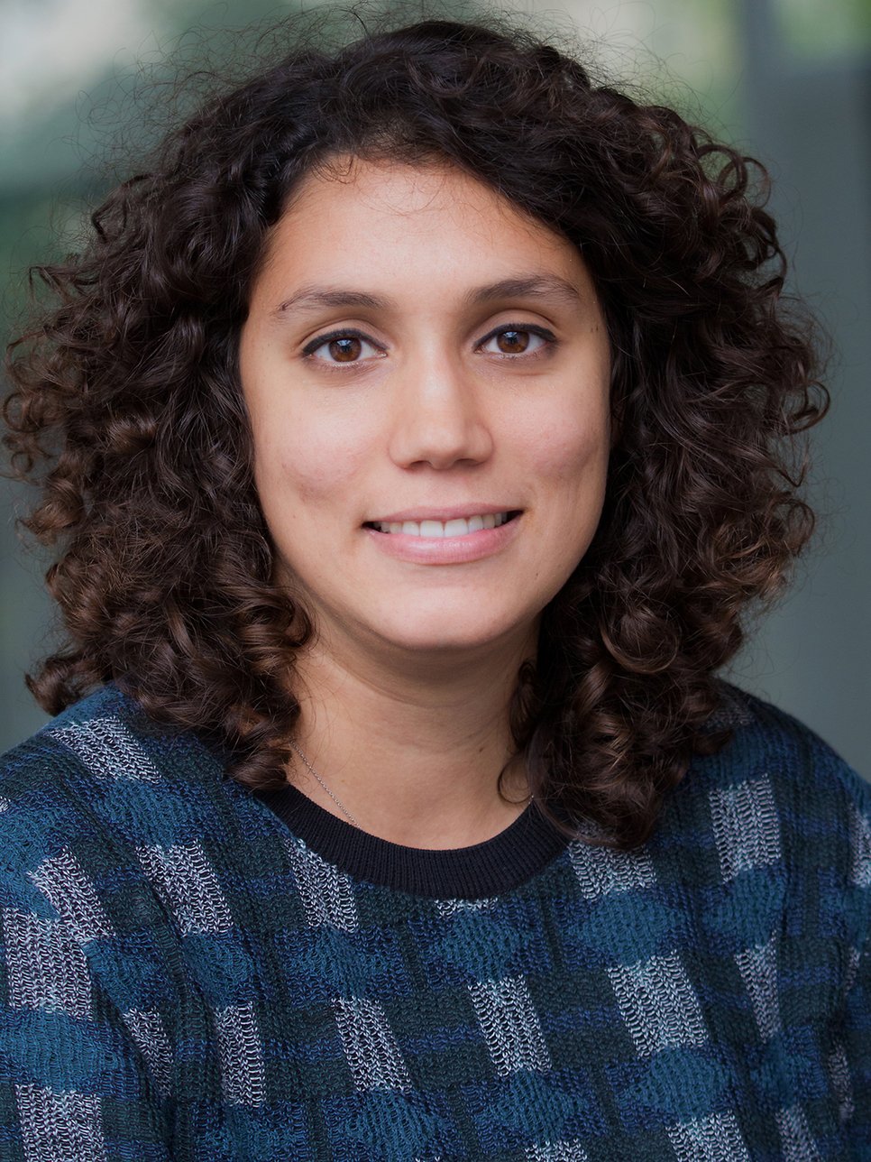 A smiling woman with dark hair wearing a black shirt, set against a blurred background.