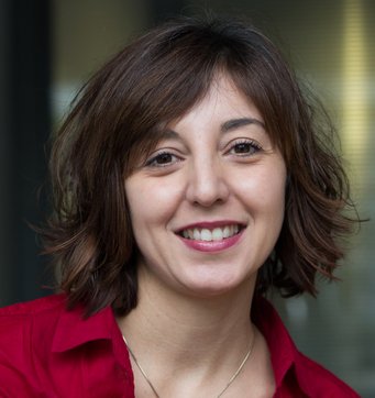 A woman with shoulder-length, wavy brown hair, wearing a red shirt, smiles at the camera.