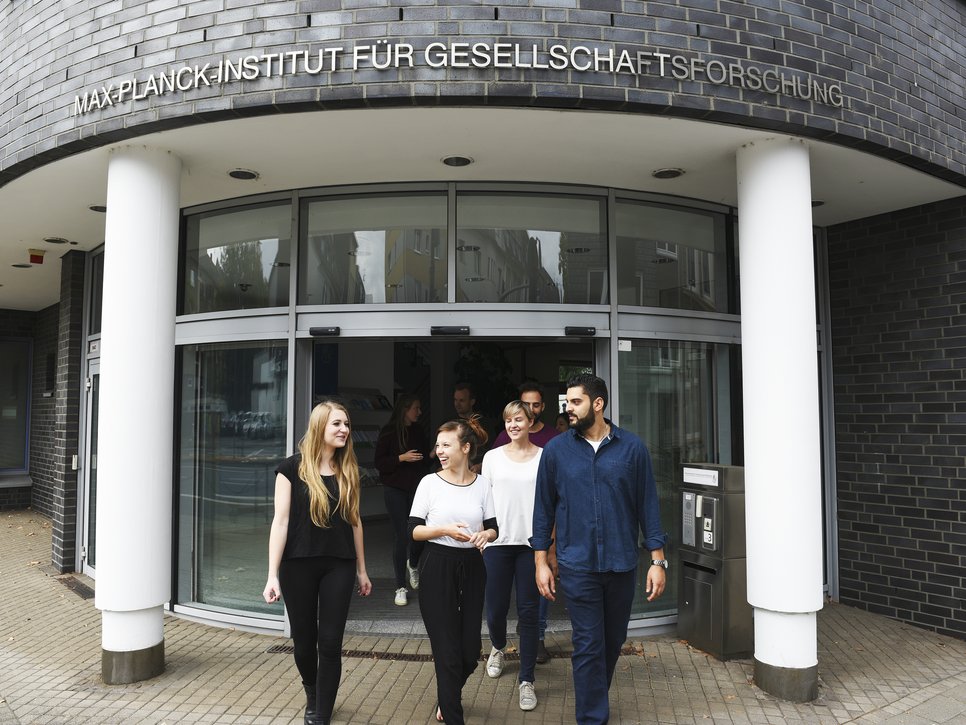 A group of people walking out of a building with a sign reading "Max Planck Institute for the Study of Societies."