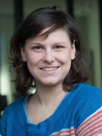 A smiling person with short brown hair, wearing a blue and striped sweater.
