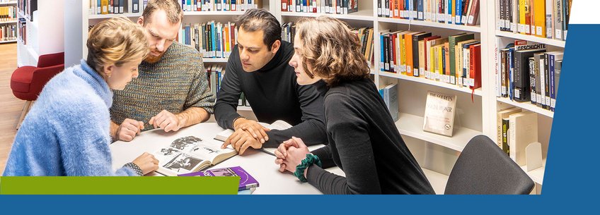 IMPRS-SPCE, Books Four people leaning over a table in a library, examining a book together. Shelves filled with books are in the background.