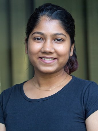 A smiling woman with dark hair wearing a black shirt, set against a blurred background.