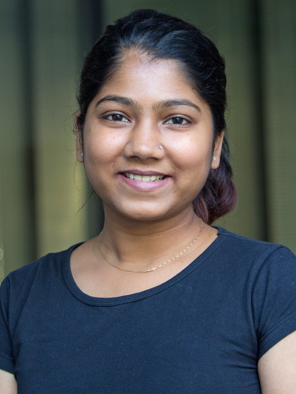 A smiling woman with dark hair wearing a black shirt, set against a blurred background.