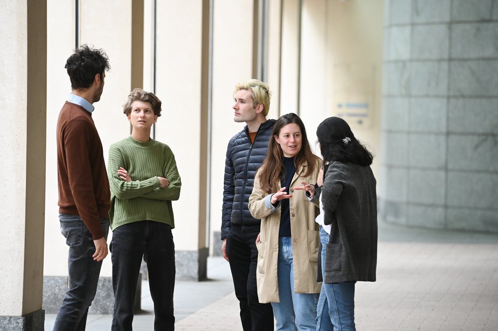 A group of five young people standing in a modern, indoor space, engaged in conversation.