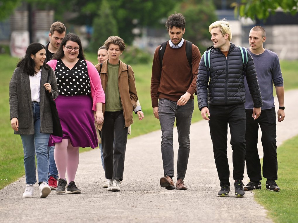 A group of seven diverse people walking together on a path in a park, wearing casual clothing and smiling.