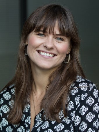 A smiling woman with long brown hair wearing a black and white floral blouse.