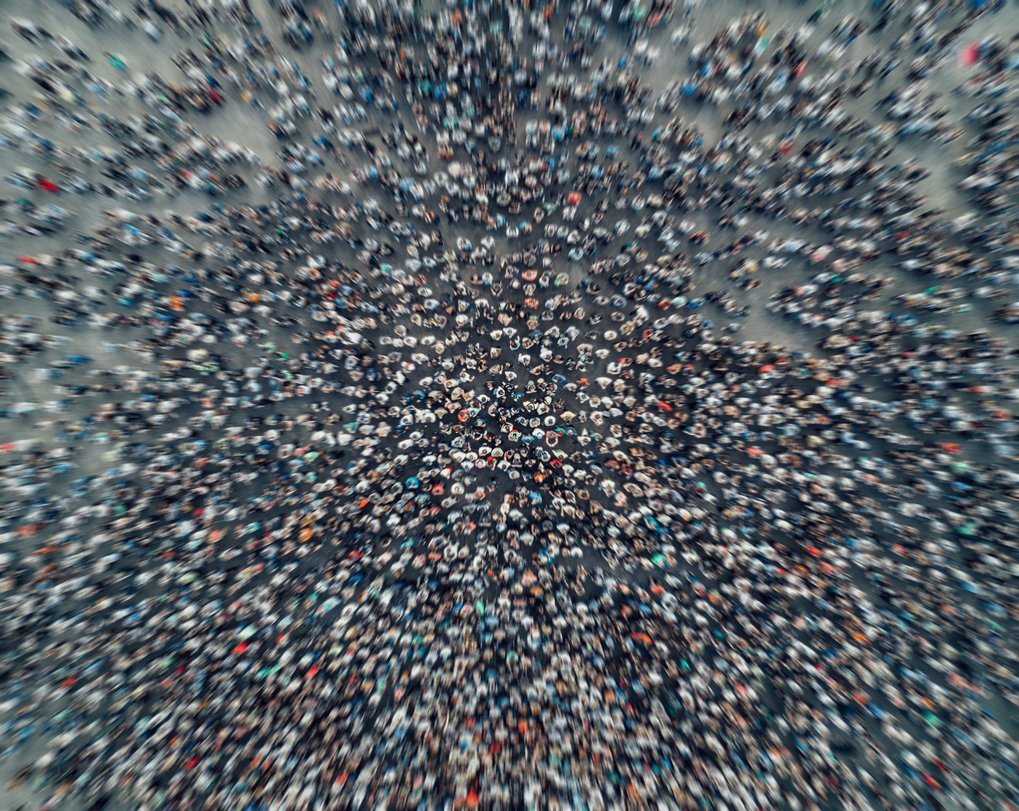 Overhead shot showing hundreds of people gathered closely together on a gray surface.
