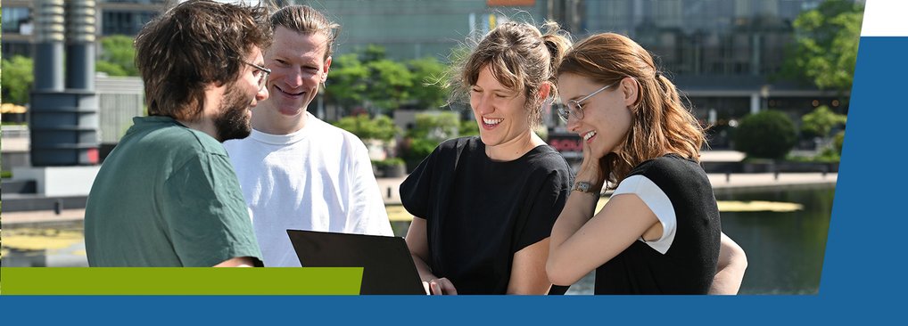 Academic Program and Approach Four individuals gather around a laptop, conversing in a park setting.