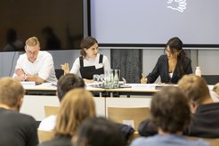 Three panelists engaged in discussion at a conference, with audience members seated in the foreground.
