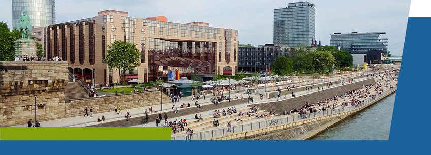 Living in Cologne A modern riverside scene featuring a mix of buildings, greenery, and people relaxing along the waterfront.