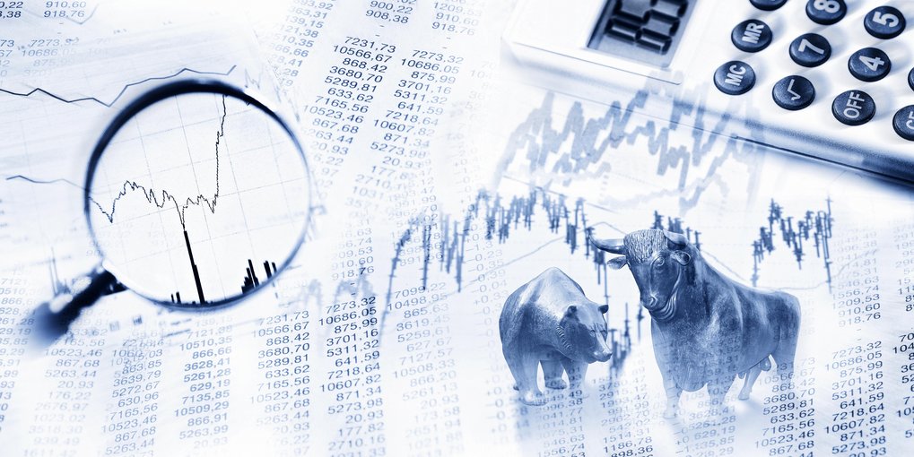 Bull and bear figurines on financial data sheets with a magnifying glass focusing on a stock graph, calculator in the background.