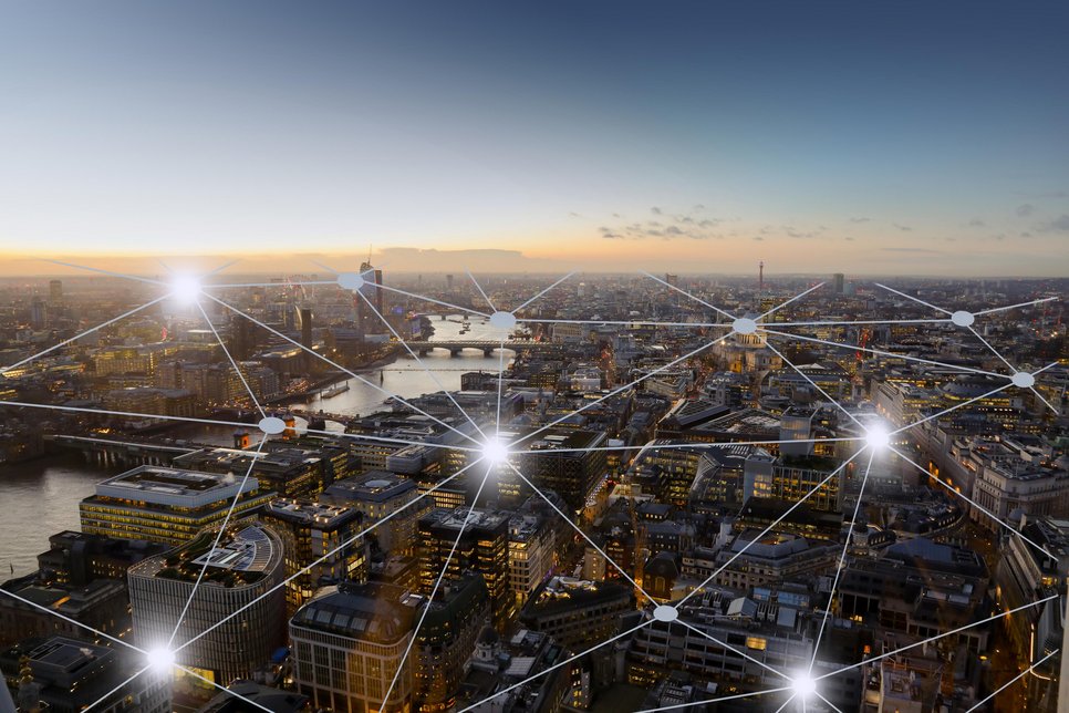 A modern cityscape at dusk, with digital nodes forming an interconnected network pattern across the sky.