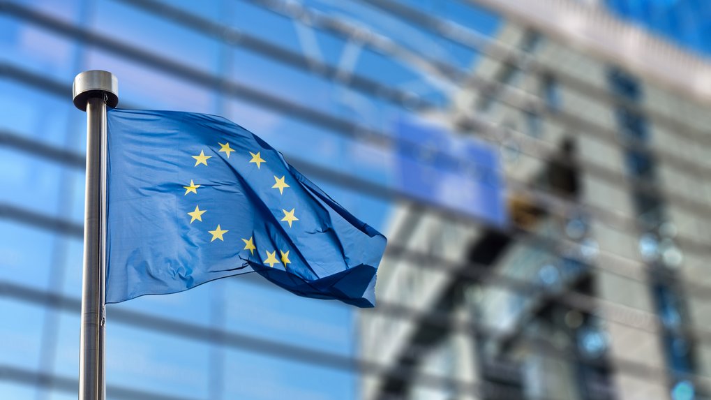 Die Flagge der Europäischen Union mit ihren zwölf goldenen Sternen auf blauem Hintergrund weht vor einem modernen Bürogebäude.