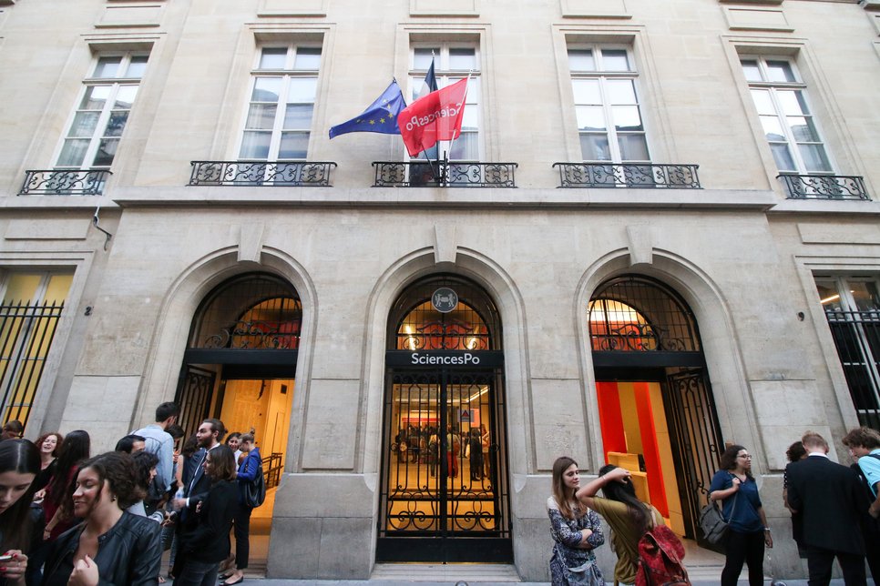 People gathered outside Sciences Po entrance, marked by European and Sciences Po flags above.