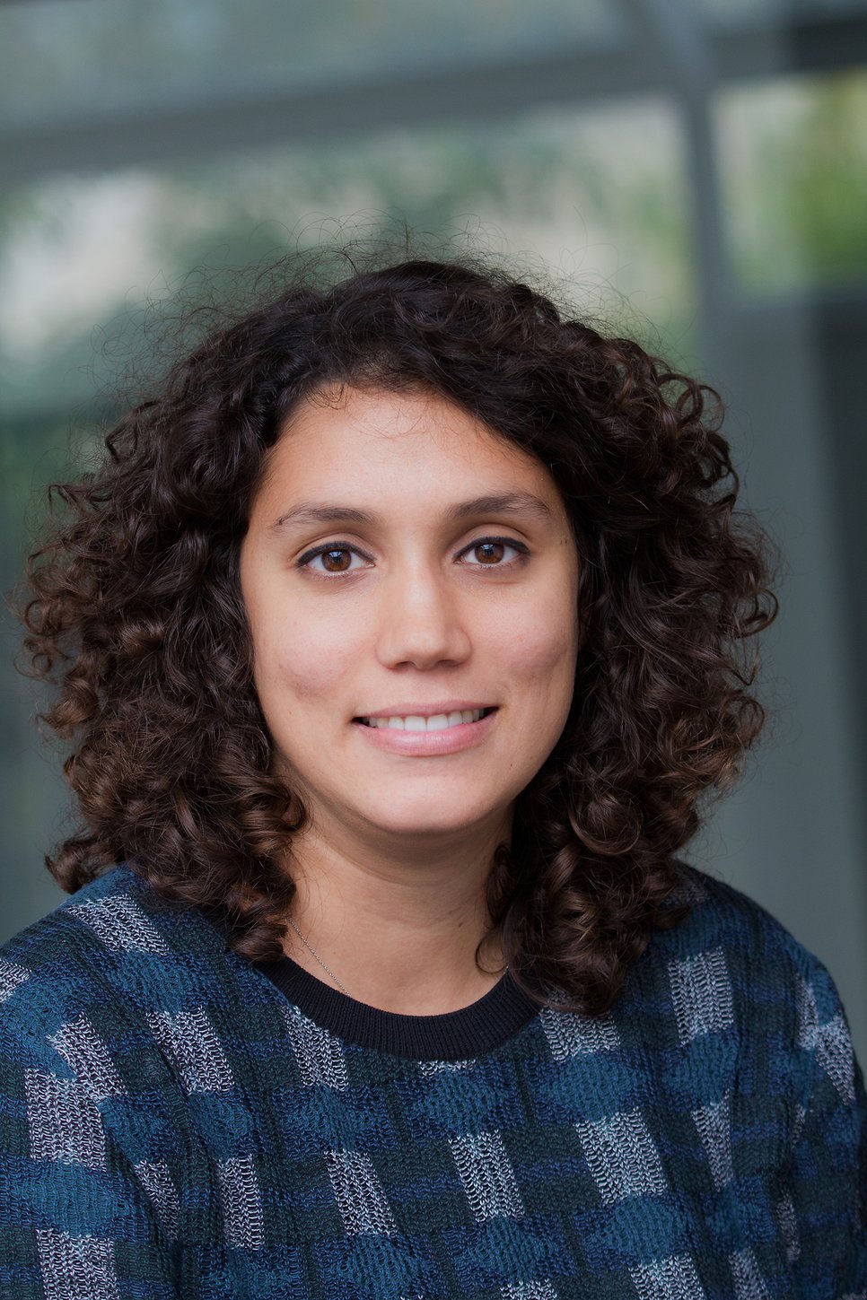 A woman with curly hair wearing a patterned sweater, smiling at the camera.