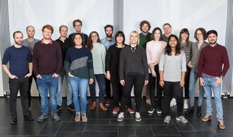 © MPIfG A group photo of 20 people standing together in a well-lit indoor space, with a neutral background.