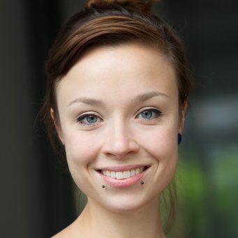 © MPIfG / Dünkelmann A close-up portrait of a woman with brown hair and blue eyes, smiling and wearing pierced earrings.