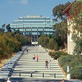 A walkway with steps leading to a modern building, surrounded by trees and people walking.