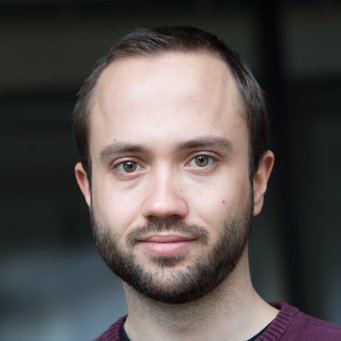 © MPIfG / Dünkelmann A close-up portrait of a man with light brown hair and a beard, wearing a maroon sweater. He has green eyes and is smiling slightly.