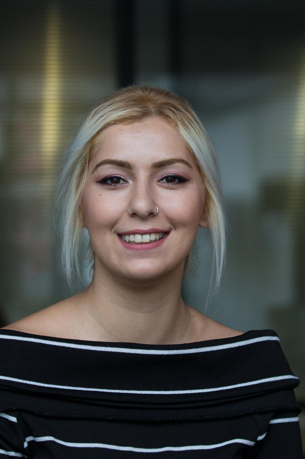 A young woman with light blonde hair, smiling, wearing a black and white striped top.