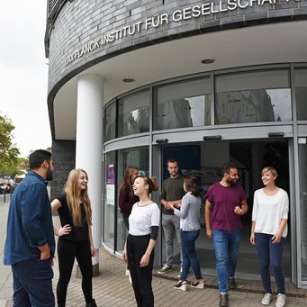 © MPIfG A group of people socializing outside a building with a sign that reads "WZB Wissenschaftszentrum Berlin für Sozialforschung."