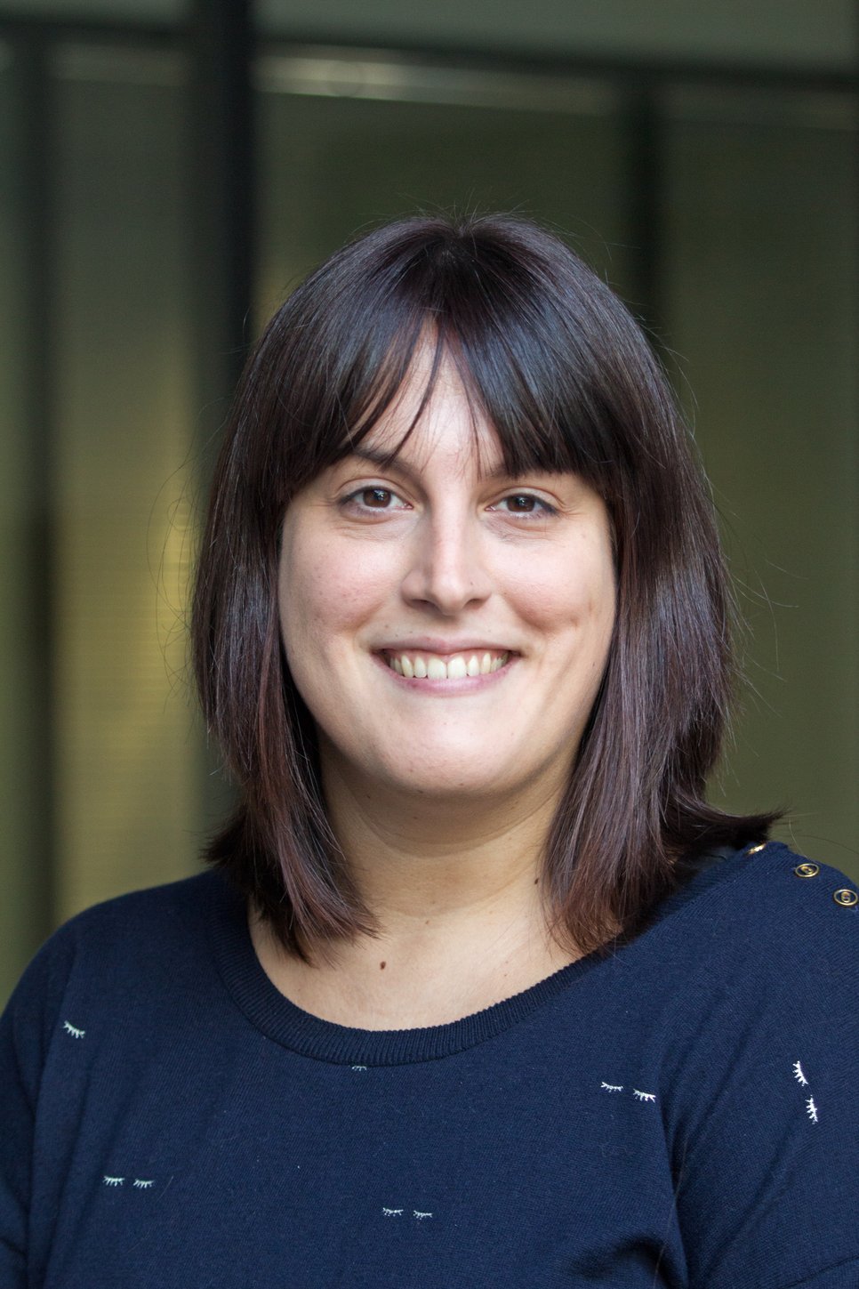 A smiling woman with shoulder-length dark brown hair, wearing a navy blue top, poses for a photo.