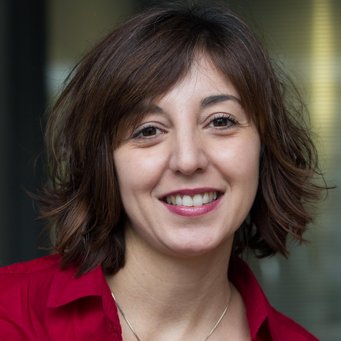 © MPIfG / Dünkelmann A smiling woman with short, wavy brown hair, wearing a red shirt, is posing for the camera.