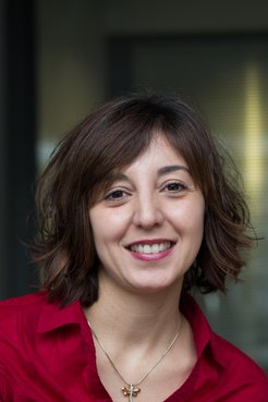 A smiling woman with short, wavy brown hair, wearing a red shirt, is posing for the camera.