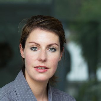 © MPIfG / Dünkelmann A woman with short brown hair and green eyes, wearing a gray button-up shirt, looking at the camera.
