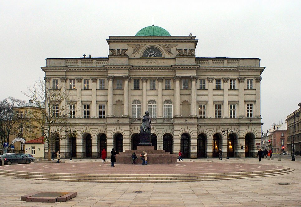 A historic building with a green dome, featuring a statue in front and surrounded by people.