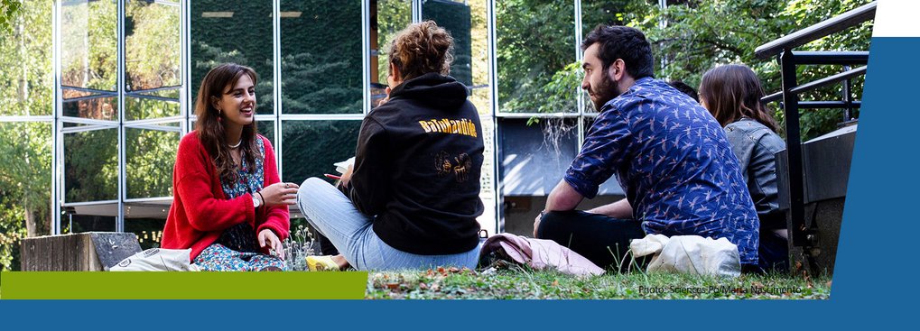 Four individuals sitting on grass near a glass building.