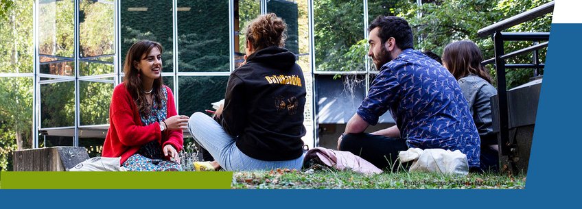 Cotutelle Four individuals sitting on grass near a glass building.