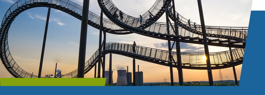 Living in Duisburg-Essen A twisted, elevated walkway resembling a roller coaster, with people walking on it against a sunset backdrop and industrial buildings in the distance.