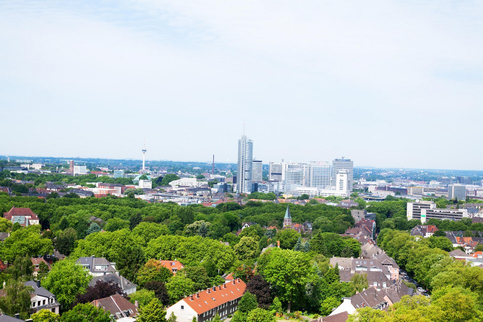 A panoramic view of the skyline of the German city Essen surrounded by greenery and blue sky.