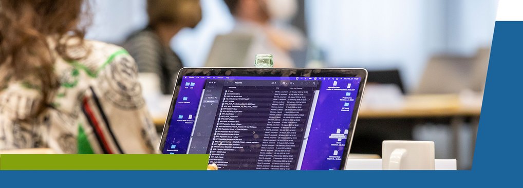 IMPRS-SPCE, Financial Support A laptop with code or software running on the screen, set in an office environment with people in the background.