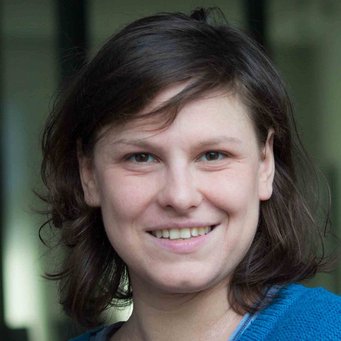 A close-up portrait of a person with medium-length brown hair, smiling and wearing a blue sweater.