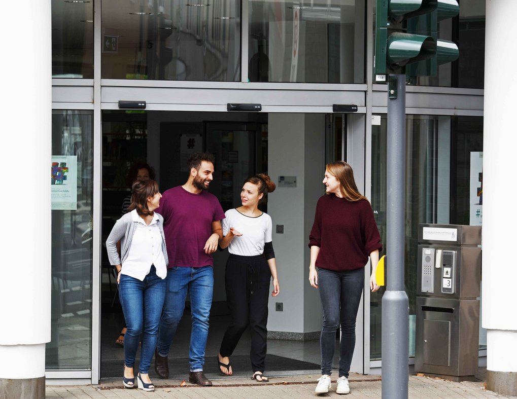 Four people are walking out of a building, engaged in conversation. They appear to be enjoying their time together.