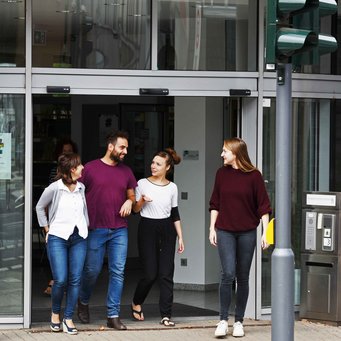 Four people are walking out of a building, engaged in conversation. They appear to be enjoying their time together.