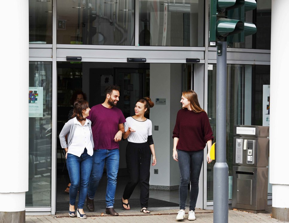Four people are walking out of a building, engaged in conversation. They appear to be enjoying their time together.
