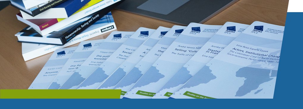 A collection of printed reports or booklets arranged in a row, with additional books stacked on the left and a laptop visible in the background.